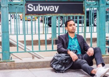 Man-sitting-under-subway-sign-wearing-earbuds