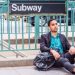 Man-sitting-under-subway-sign-wearing-earbuds